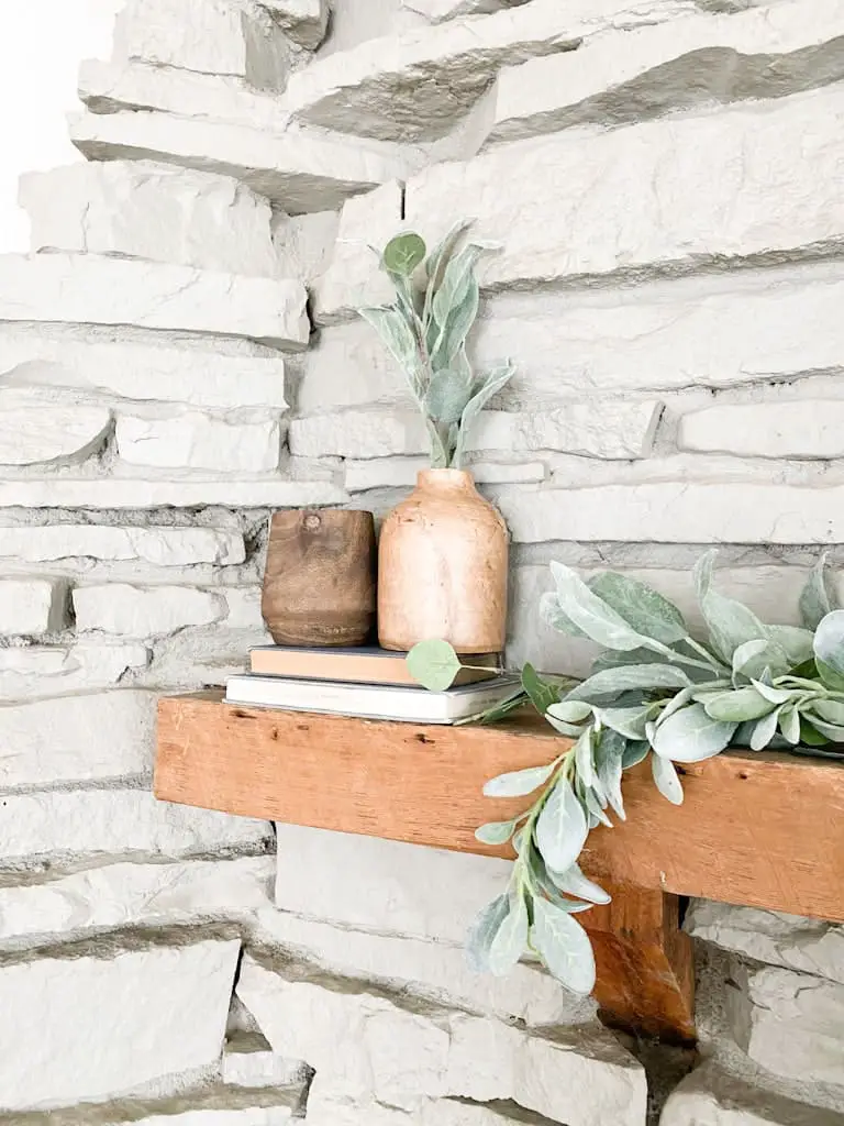 A wood fireplace mantel with two different toned wood vases on top of a stack of 2 old books.