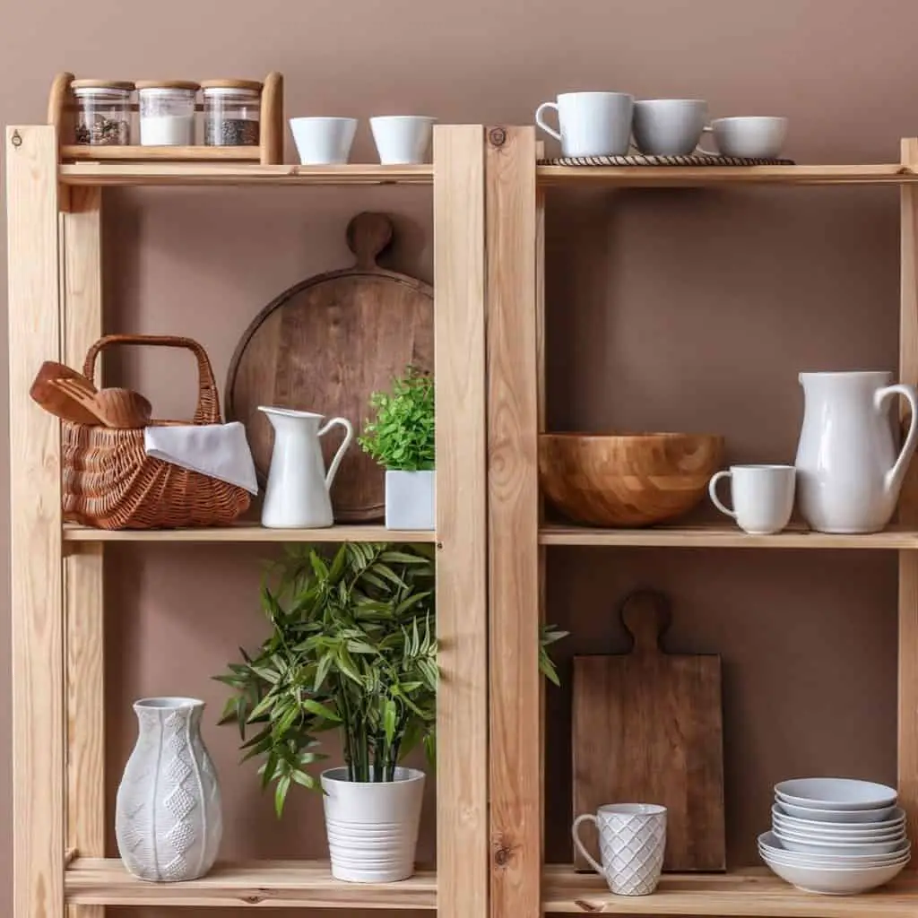 Wooden shelves with a variety of white kitchen ware mixed with wood kitchen items and 2 plants in white pots.