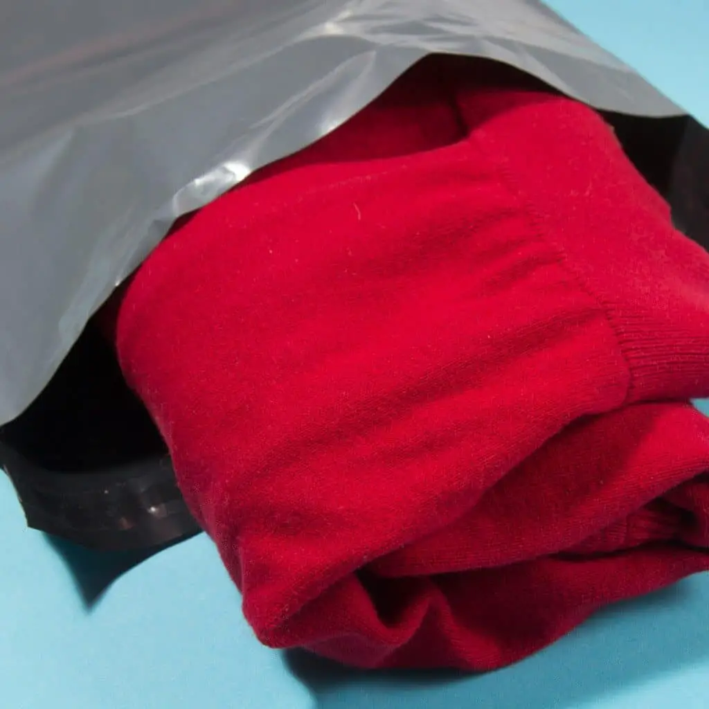 A folded red sweater being placed in a gray plastic mailer.