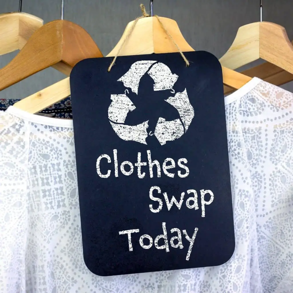 A white shirt on a wooden hanger with a sign in front of it that says "clothe swap today" with a recycle sign at the top.