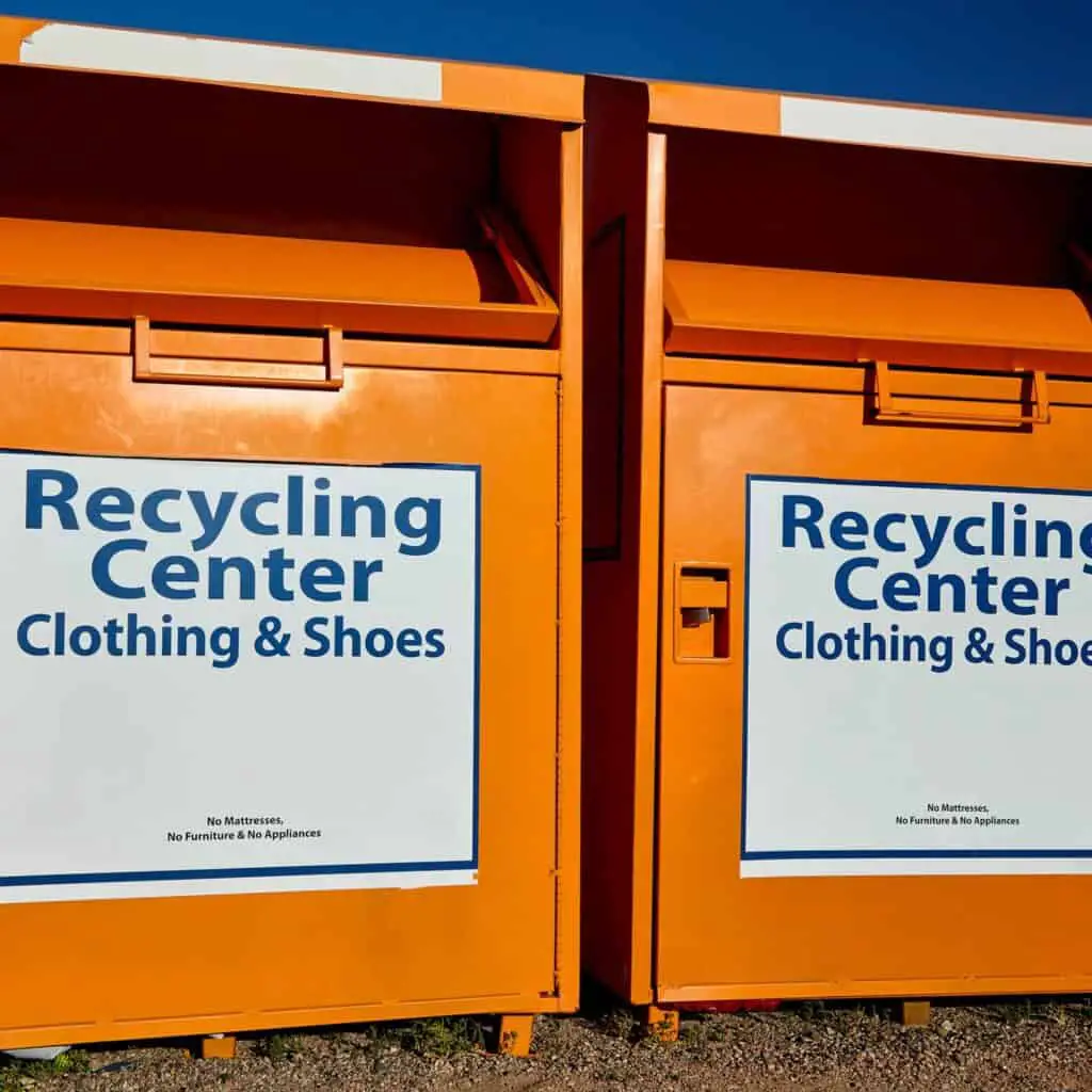 2 orange metal bins with signs that say "recycling center, Clothing and shoes." Recycling old clothes by dropping them off at clothing recycling bins.