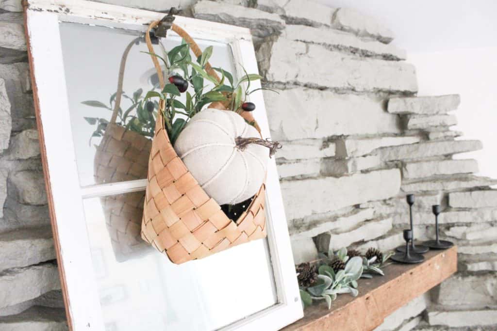 A cute little fabric pumpkin over a bed of olive branch stems sit in this adorable hanging basket. A great way to add some color to your neutral fall decor.