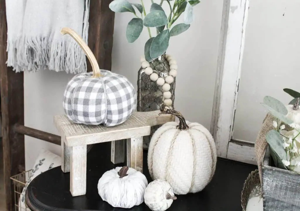 This cute collection of neutral fall decor has varying sizes, heights, and materials. I love the warmth the gingham and knit pumpkins bring while the textures of he other 2 textures add more visual interest. the touch of green with the lambs ear and the wood from the little mini stool and vintage ladder add nice touches of color.