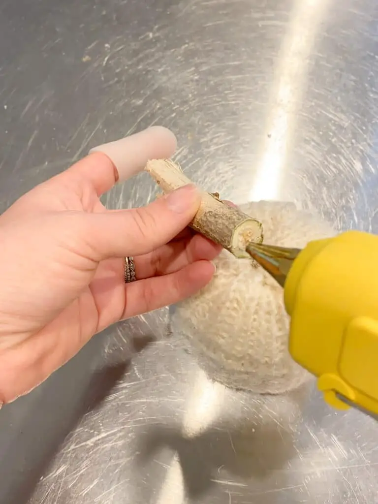 Photo shows how I used my hot glue gun to glue a stick to the top of my DIY sweater pumpkin as the stem.