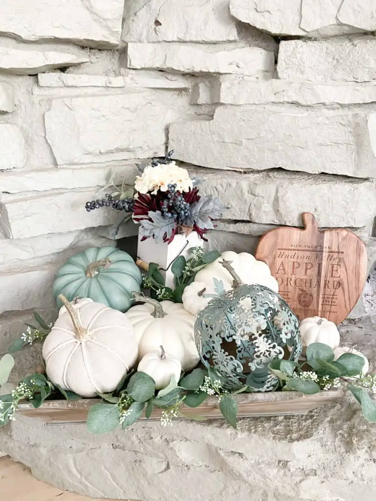 Muted fall decor, a collection of white and heirloom pumpkins mixed with eucalyptus leaves in a wooden tray. A fall bouquet of flowers with a wooden apple orchard sign.