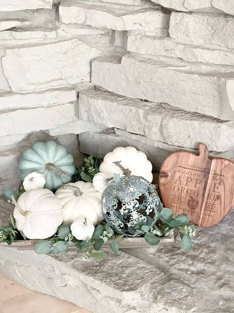 Muted fall decor, a collection of white and heirloom pumpkins mixed with eucalyptus leaves in a wooden tray. A wooden apple orchard sign.