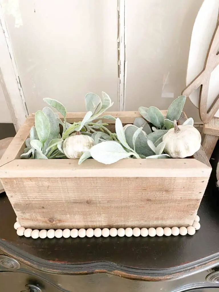 Neutral fall decor, a wooden box with a wood bead garland trim, filled with faux lamb's ear and mini white pumpkins.