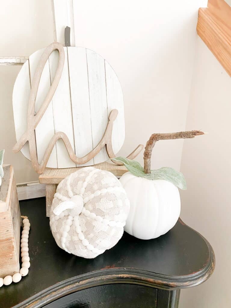 Neutral fall decor, a white pumpkni with a stick stem, a gray and white patterned fabric pumpkin, a white wood pumpkin sign with a wood "hi" in front of it.