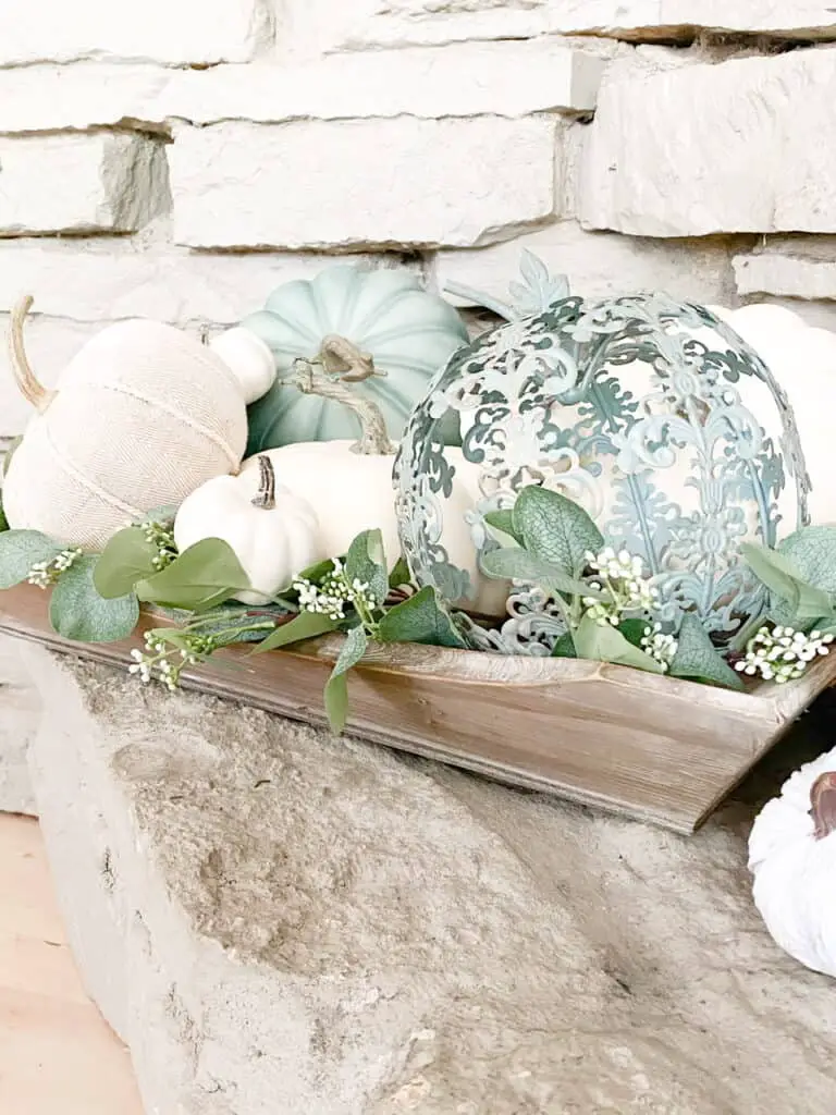 Muted fall decor, a collection of white and heirloom pumpkins mixed with eucalyptus leaves in a wooden tray. A wooden apple orchard sign.