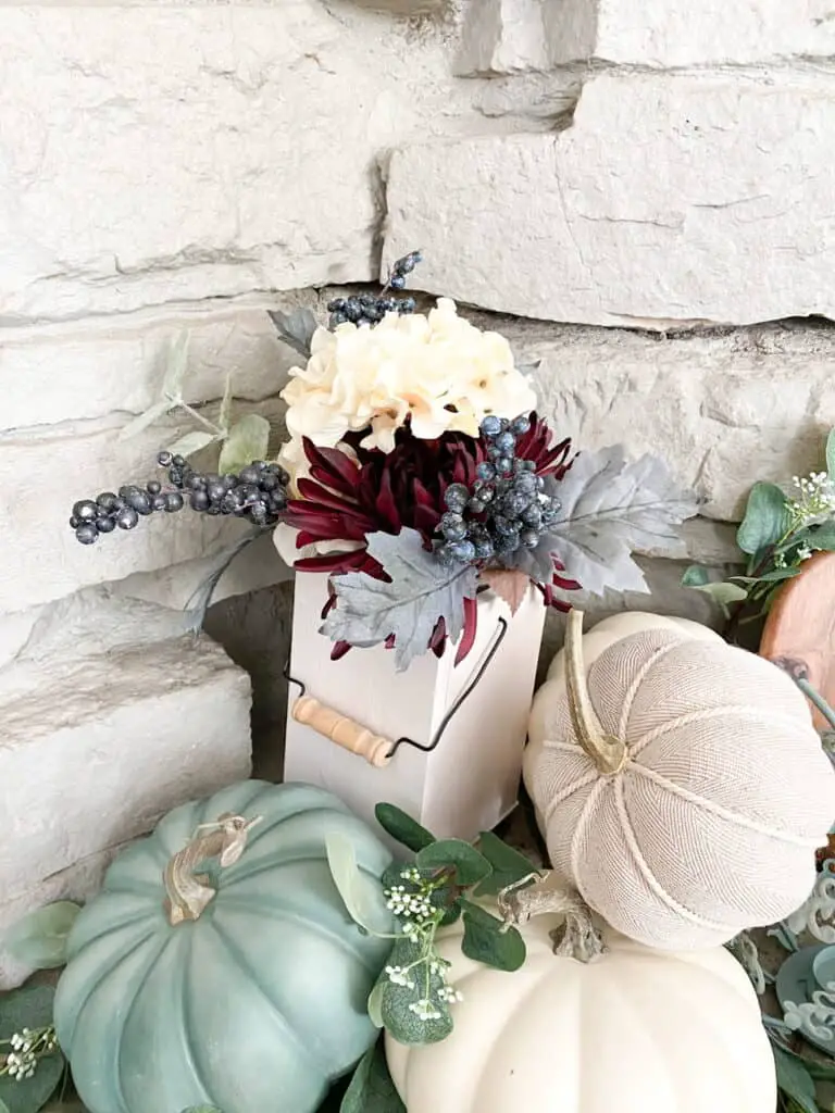 Muted fall decor, a collection of white and heirloom pumpkins mixed with eucalyptus leaves in a wooden tray. A fall bouquet of flowers in a white wooden lantern.