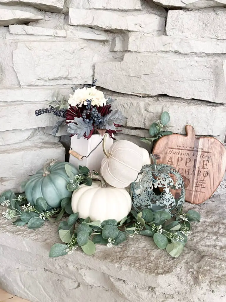 Muted fall decor, a collection of white and heirloom pumpkins mixed with eucalyptus leaves in a wooden tray. A fall bouquet of flowers with a wooden apple orchard sign.