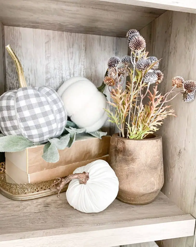 Bookshelf fall decor, a collection of different neutral pumpkins on some stacked books in a tray and a wooden vase with some fall stems inside.