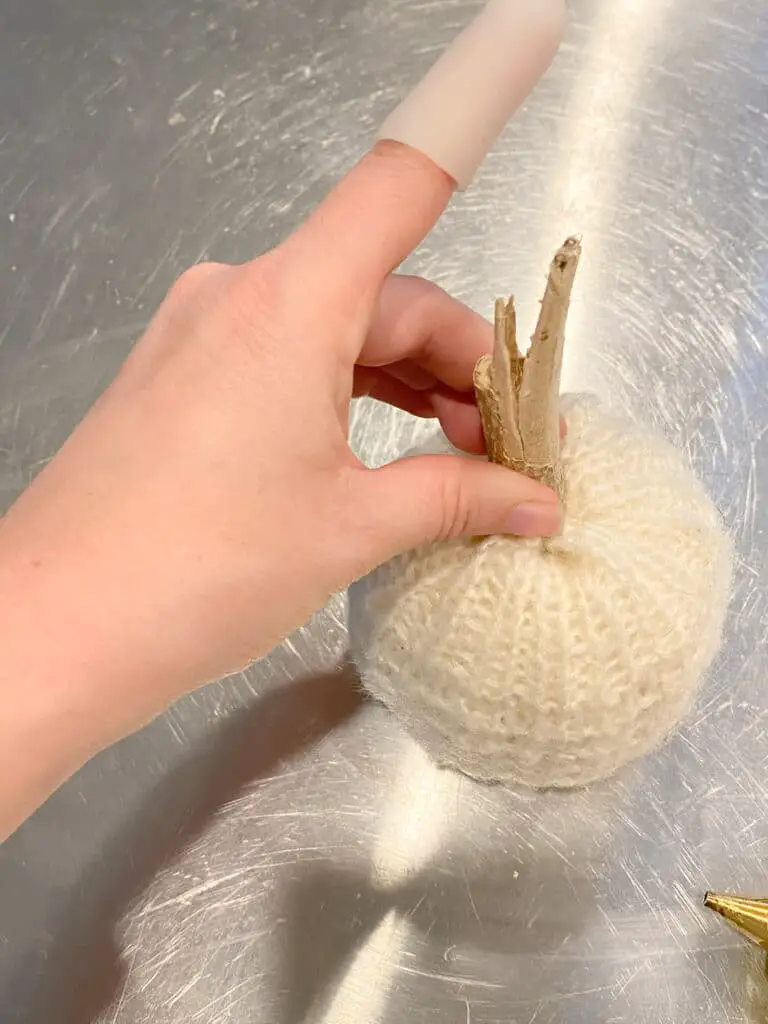 Photo shows how I used my hot glue gun to glue a stick to the top of my DIY sweater pumpkin as the stem.