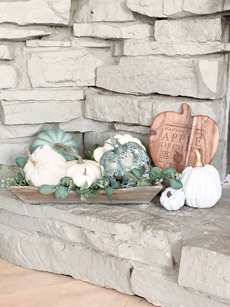 Muted fall decor, a collection of white and heirloom pumpkins mixed with eucalyptus leaves in a wooden tray. A wooden apple orchard sign.