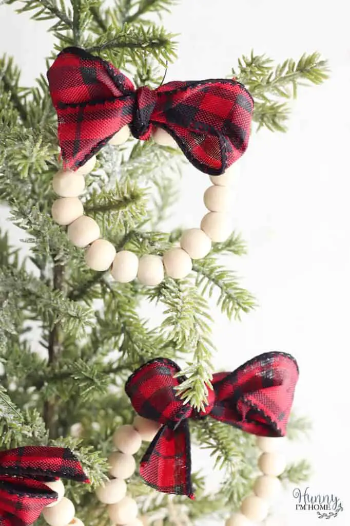 Wood bead wreath ornaments with red and black plaid ribbon hanging on a Christmas tree,