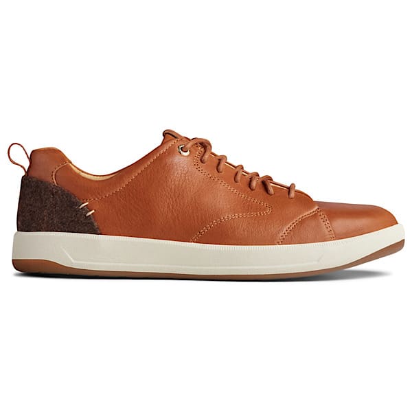 A men's sneaker from Sperry, that is light brown keather with a white sole, and a fabric patch on the heel.