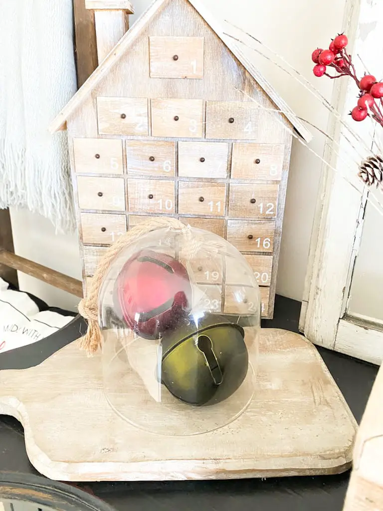 These vintage bells in red and green under a glass cloche sitting on a wood paddle cutting board add a great pop of color to these neutral Christmas decorations. Behind that display is a wooden house advent calendar.