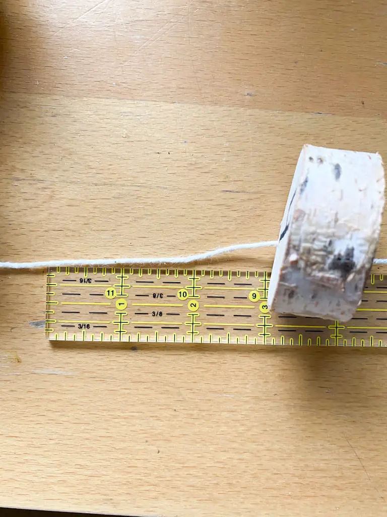 Measure and cut 12 inches of string to hang the slices of wood.