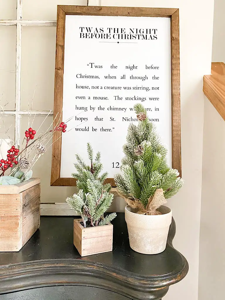 2 mini faux pine trees, one in a wood box and the other in a ceramic pot are in front of a wood framed sign with a passage from The Night Before Christmas.