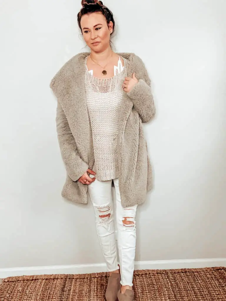 This cozy winter outfit is made up of a gray teddy style jacket, a gray open knit sweater, some white distressed skinny jeans, a gold medallion necklace, and some taupe booties.