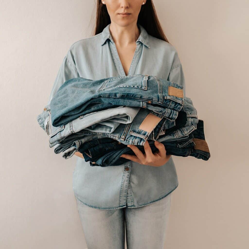 Photo shows a woman dressed in all denim holding a plie of jeans,