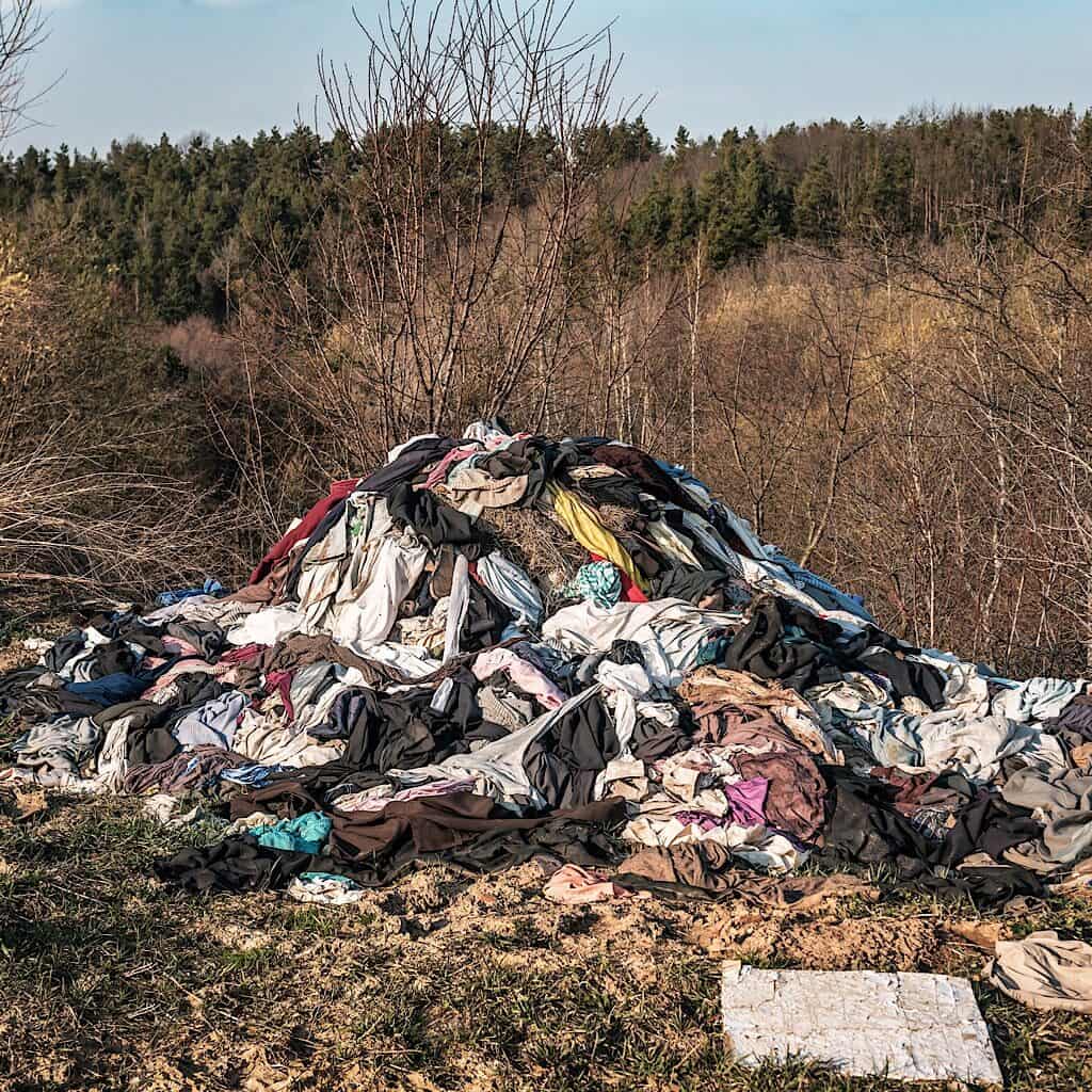 This photo of a pile of clothes that have been thrown in a landfill is a great example of what we want to avoid. one of the benefits of shopping second hand is you are saving items from being thrown into landfills.