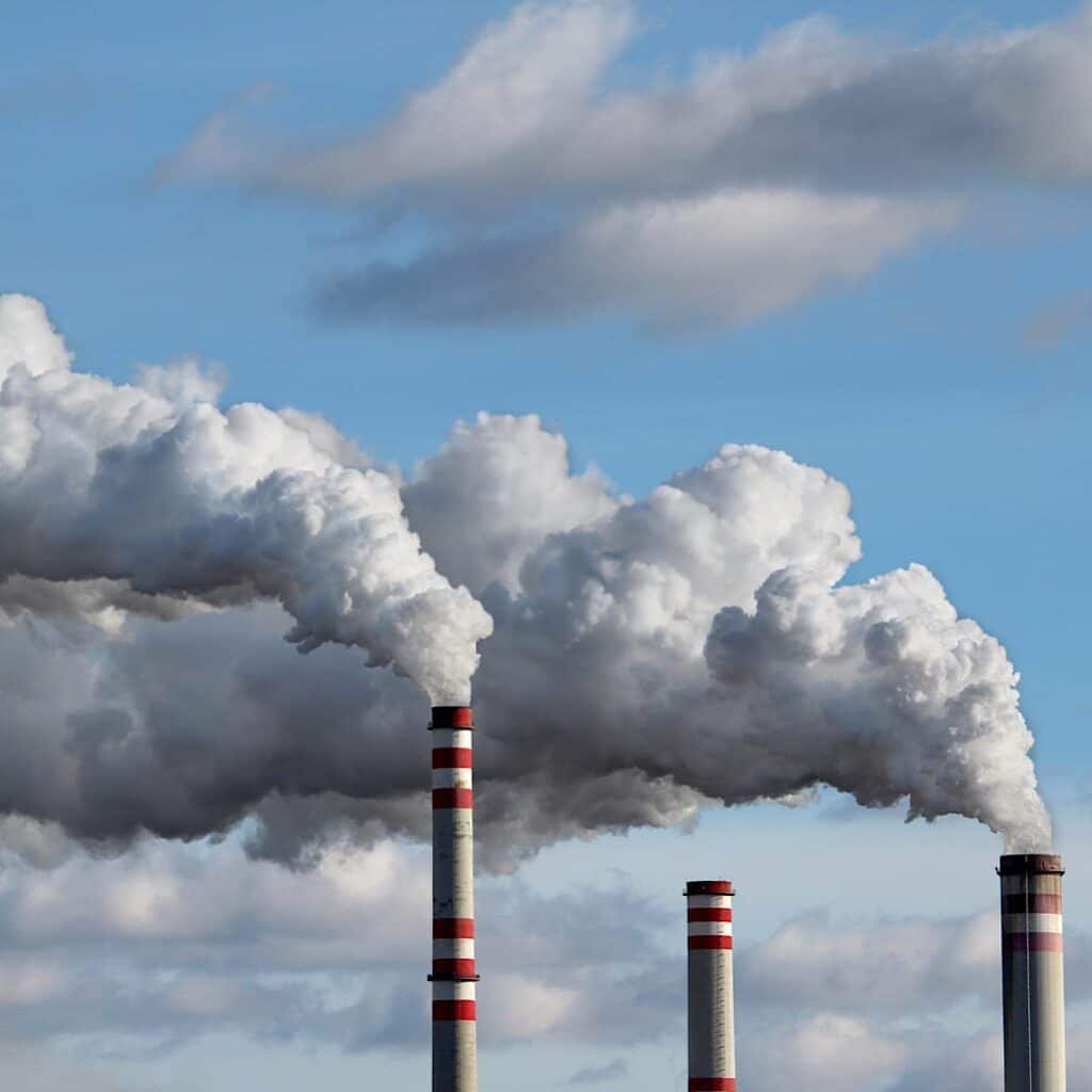 Photo shows 3 smoke stacks releasing pollution into the air. One of the benefis of shopping second hand is that you lessen he demand for new clothing and can help to reduce the amount of pollution released from its production.