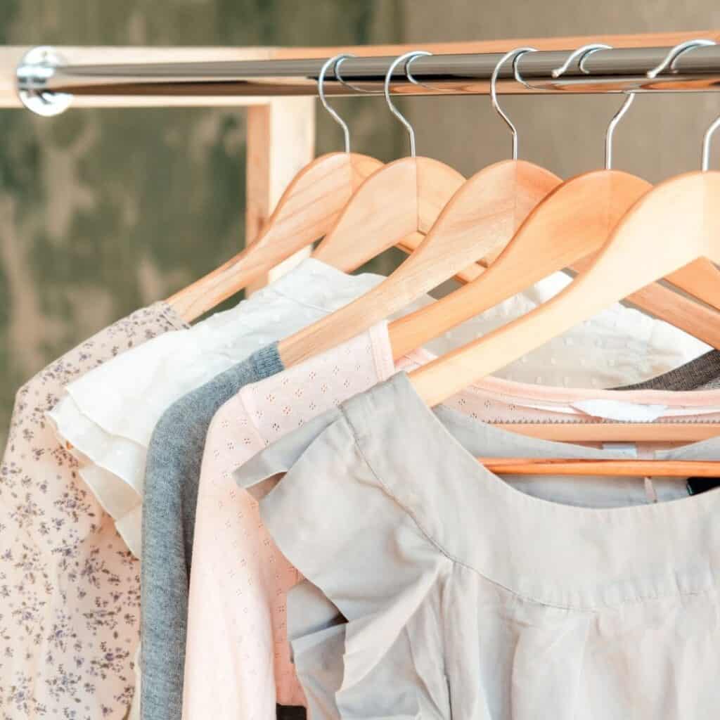 Different style tops in blush pinks and light blues hanging on a rack.