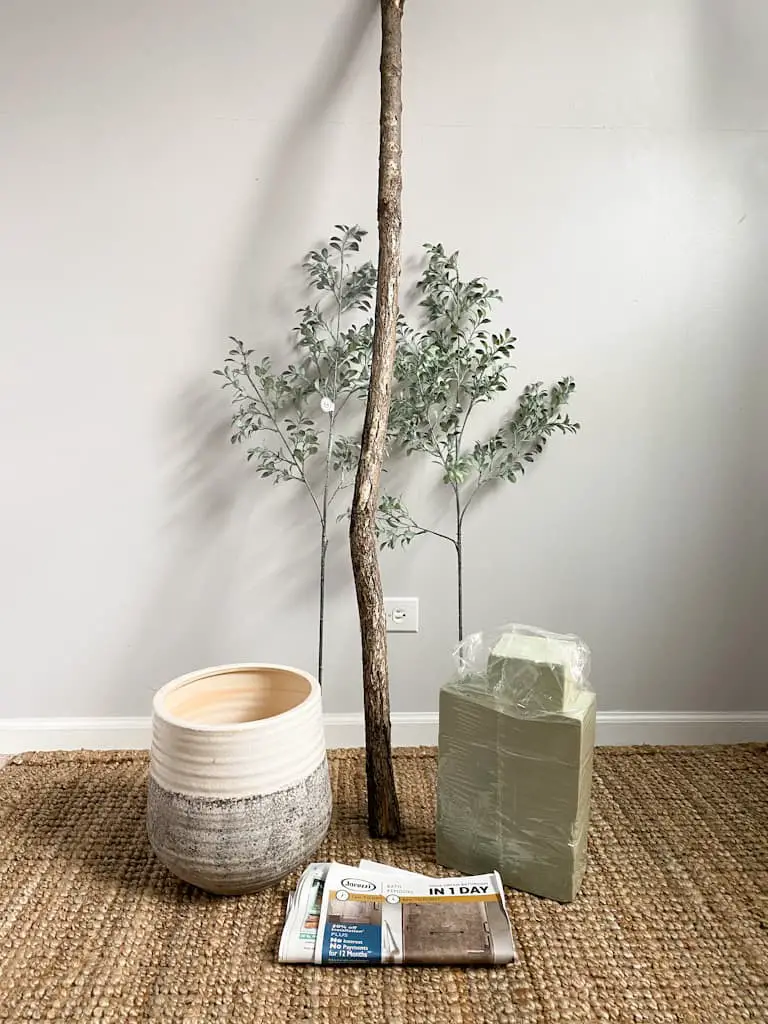 Some of the supplies you will need to make a fake tree including, a tree branch, some fake greenery stems, blocks of floral foam, and some recycled newspaper.