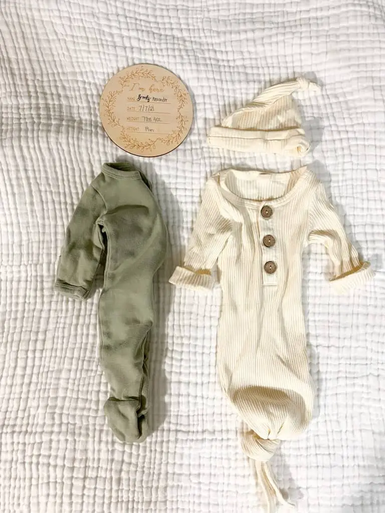 This is what's in my hospital bag for baby. A sage green zip up sleeper for bring baby home, a cream knotted gown that is ribbed with wooden buttons and a matching hat, and a wooden sign that lists baby's name (Brooks Alexander), height, weight, and date of birth to use when taking pictures after baby is born.