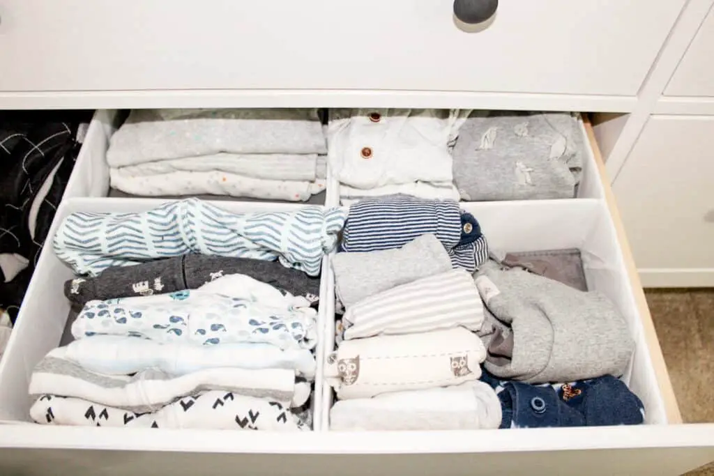 A dresser drawer with drawer organizers that house baby pajamas and one piece outfits.