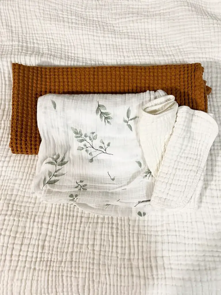 This is what's in my hospital bag for baby. A rust orange waffle blanket, a muslin swaddle blanket that is white with green leaves on it, and 2 white muslin burp cloths.