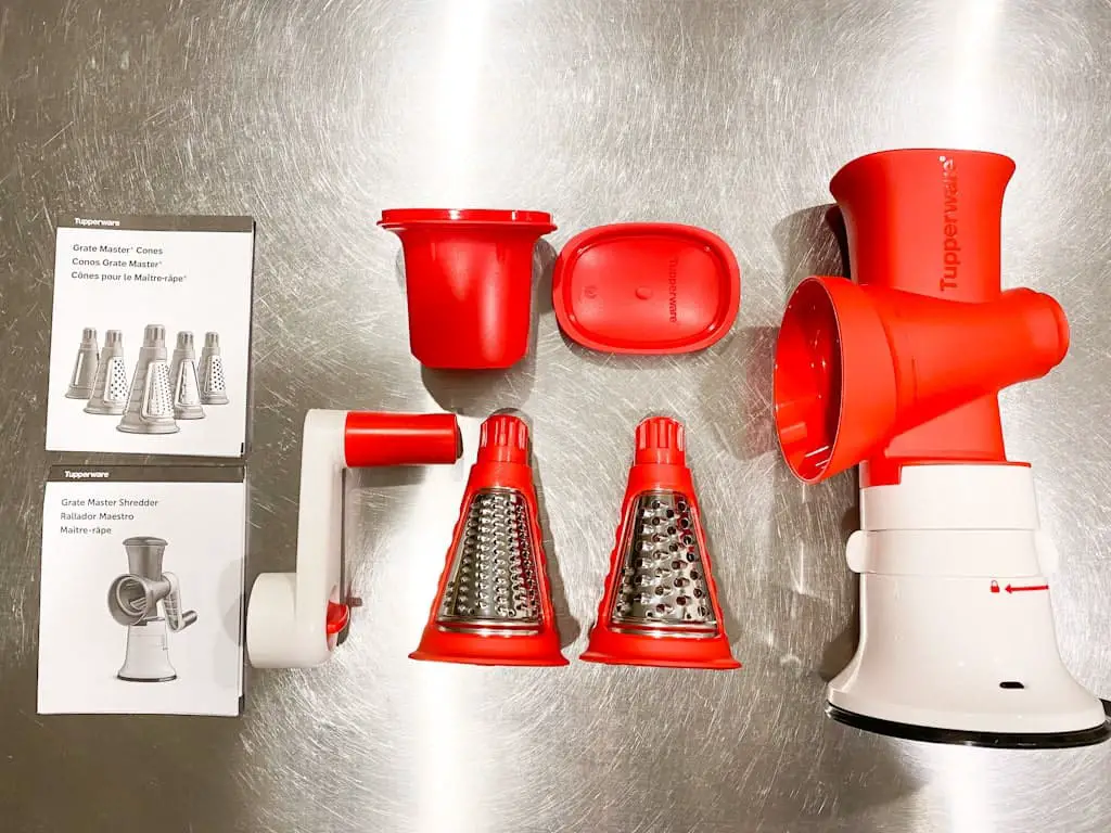 The Tupperware Grate Master Shredder is another must have Tupperware product. Image shows the product comes with a base, 2 grating cones (one fine and one coarse), the plunger to push food down, the handle to turn the grating cones, and instruction manuals.