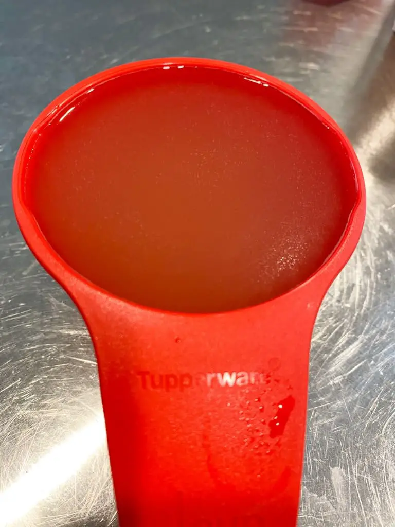 A 1 cup measuring mate filled with chicken stock. The measuring mate has a left and right handed pour spout.