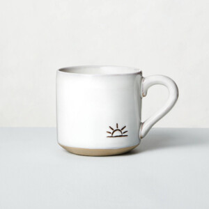 A white and tan ceramic mug with a sunrise engraved on it.