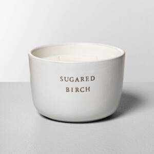 A candle in a white ceramic bowl with the words sugared birch on it.