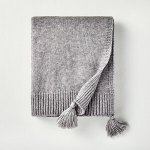 A gray knit throw blanket with tassels.