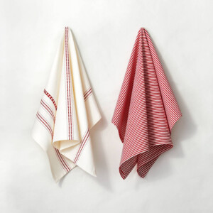 2 tea towels hanging on a wall. One is mostly cream with a red pattern striped down in a few places. The second is red and white thin stripes.