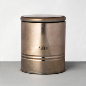 A candle inside a metal tin with the word aspen engraved on the front.