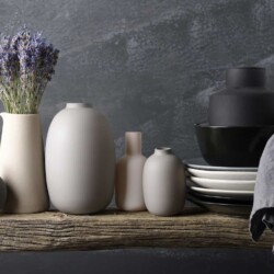 Find out the answer to your own "What is my decorating style?" question and learn how to create a home you love. Image shoes assorted neutral colored pottery, one has a bunch of lavender in in, some white and black plates in a stack with a black bowl and a black vase on top, all on a weathered wood bench.