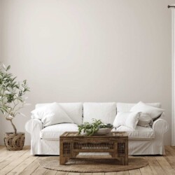 Find out the answer to your own "What is my decorating style?" question and learn how to create a home you love. This photo shows a cozy neutral living room with wood accents. it is a mix of modern farmhouse and bohemian styles. There is a white plush slip cover couch with big white pillows, a wood boho style coffee table with a large stone bowl with plants in it, it sits on top of a woven rug, there is a potted tree in a wicker basket in the corner.