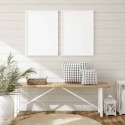 Find out the answer to your own "What is my decorating style?" question and learn how to create a home you love. Image shows a white and natural wood bench with a small basket tray and 2 gingham print pillows on it in front of a shiplap wall which has 2 large white frames that are empty. There is a tan woven rug, 2 white lanterns of different sizes, and a large potted plant in an antique looking ceramic pot.